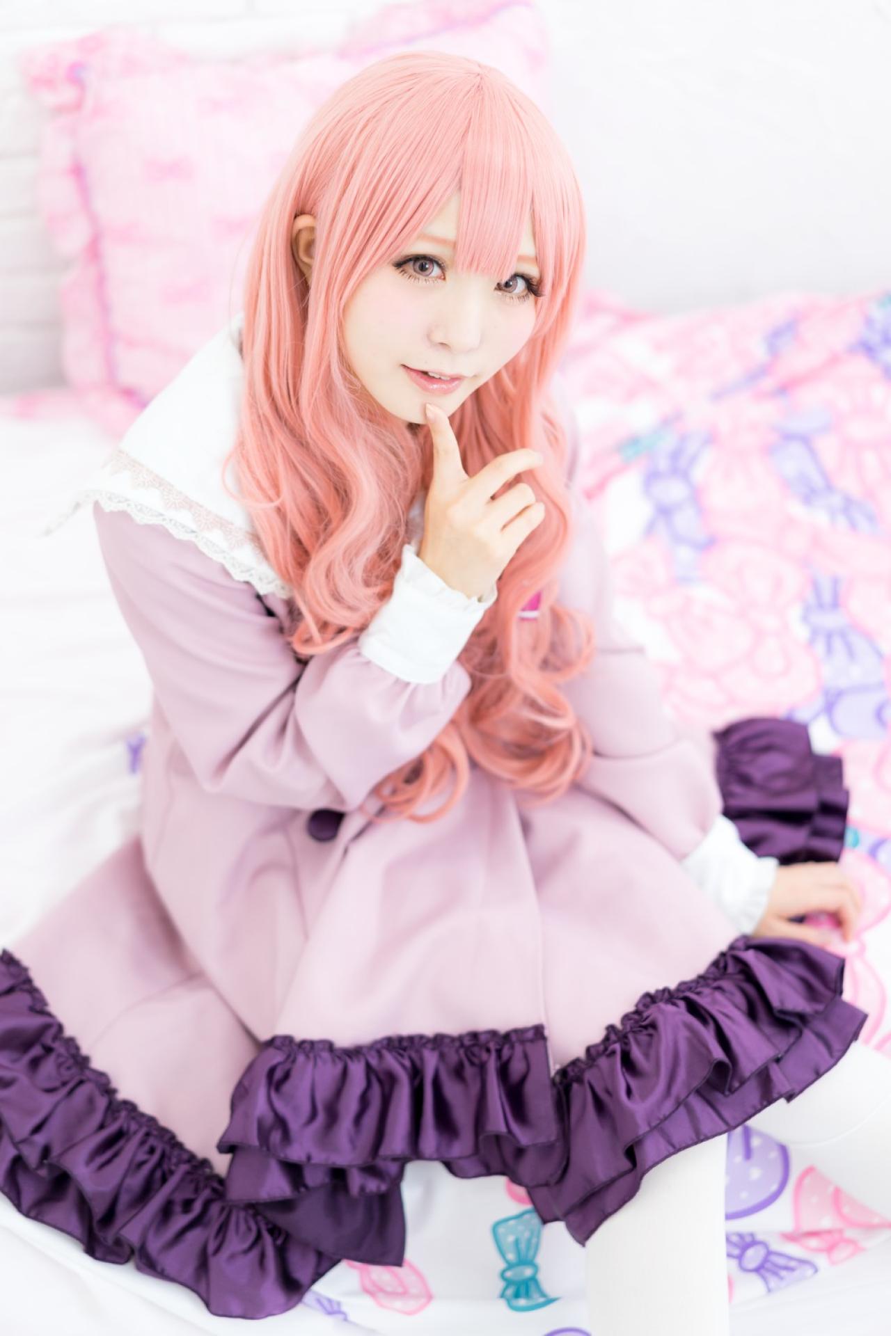 茉夏扮袴田日向坐在床上，右手食指贴着下巴，作嘘手势卖萌，左手搭在裙摆上