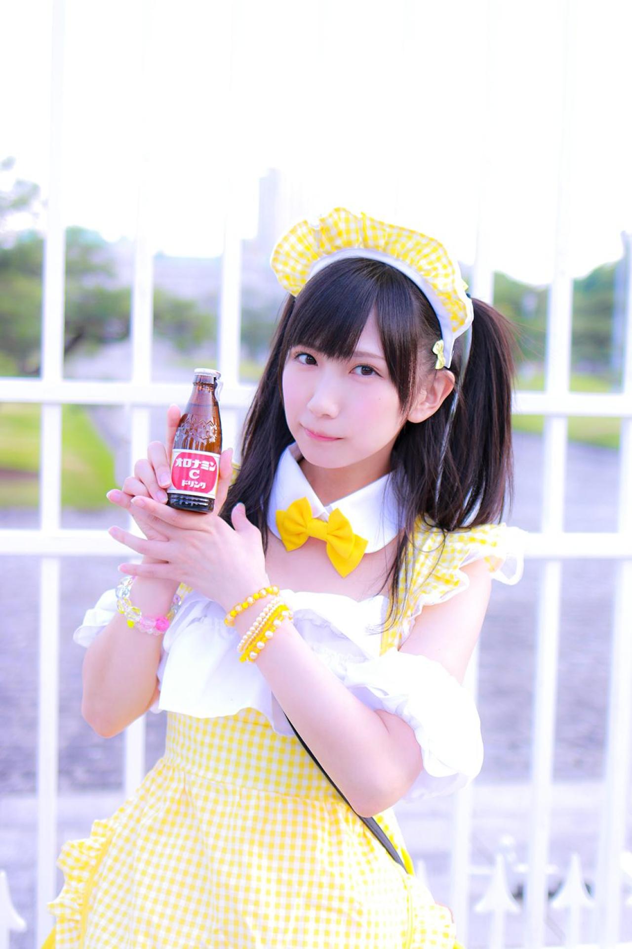 小日向くるみ扮女仆双手捧着ORONAMIN C（オロナミンC）饮料，抿嘴卖萌，站在栏杆前 正面