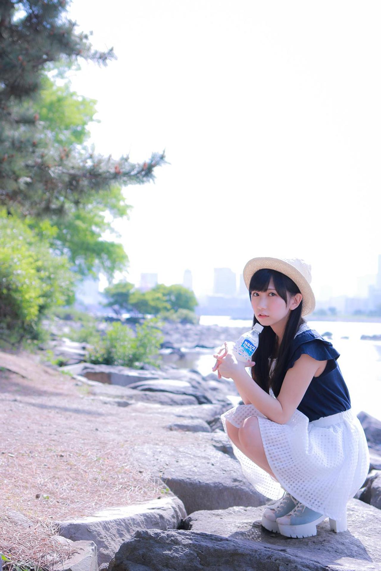 小日向くるみ双手捧着可尔必思饮料，轻抵下巴，蹲在河边