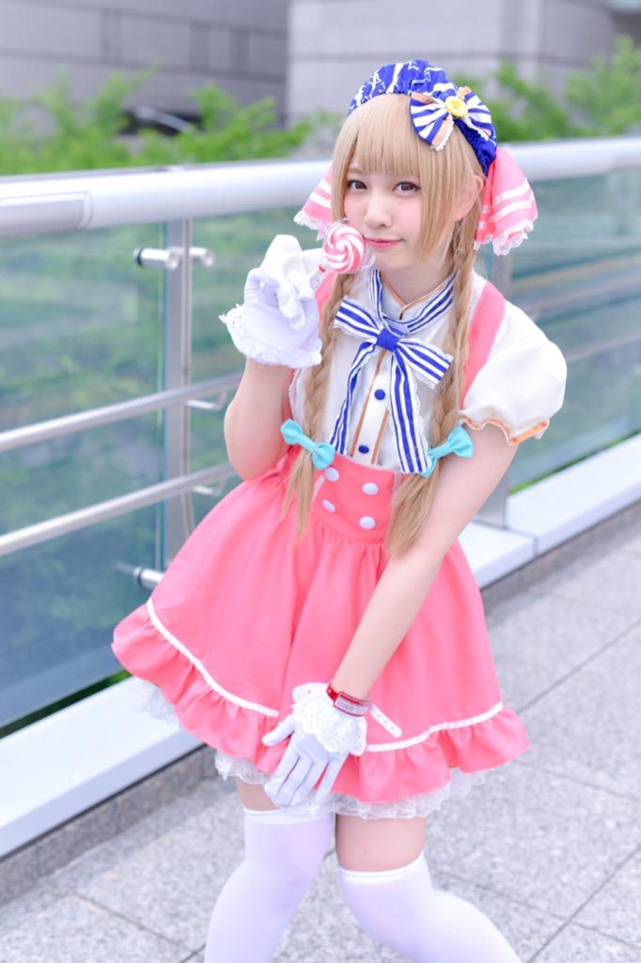 玖音さん扮南小鸟右手拿着棒棒糖，左手轻扶裙摆站在栏杆旁