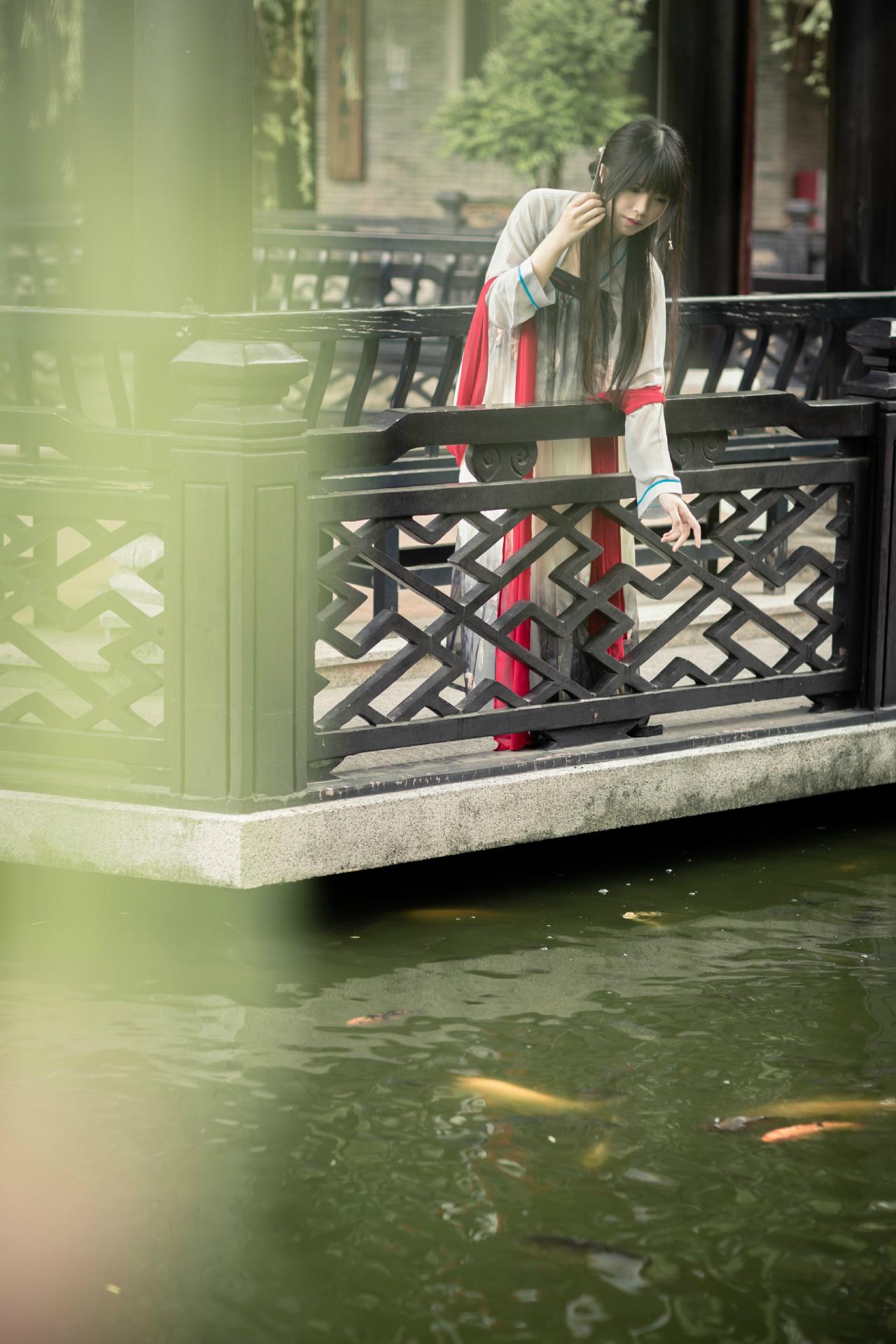 安姐姐轻抚发梢，站在亭廊，看着湖里的红金鱼