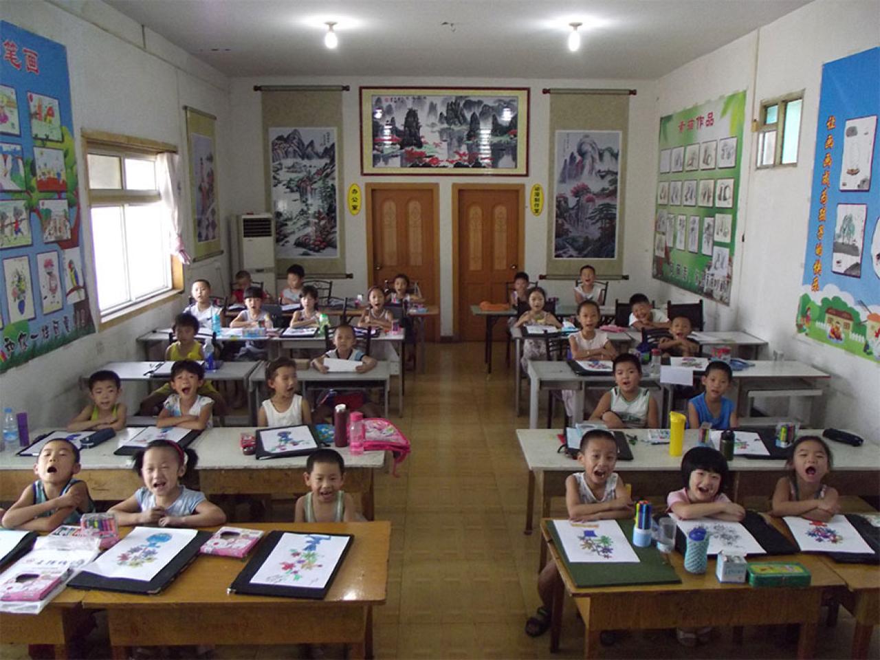 圆梦画室初小班同学在画夹上作画，开心大笑的课堂情景