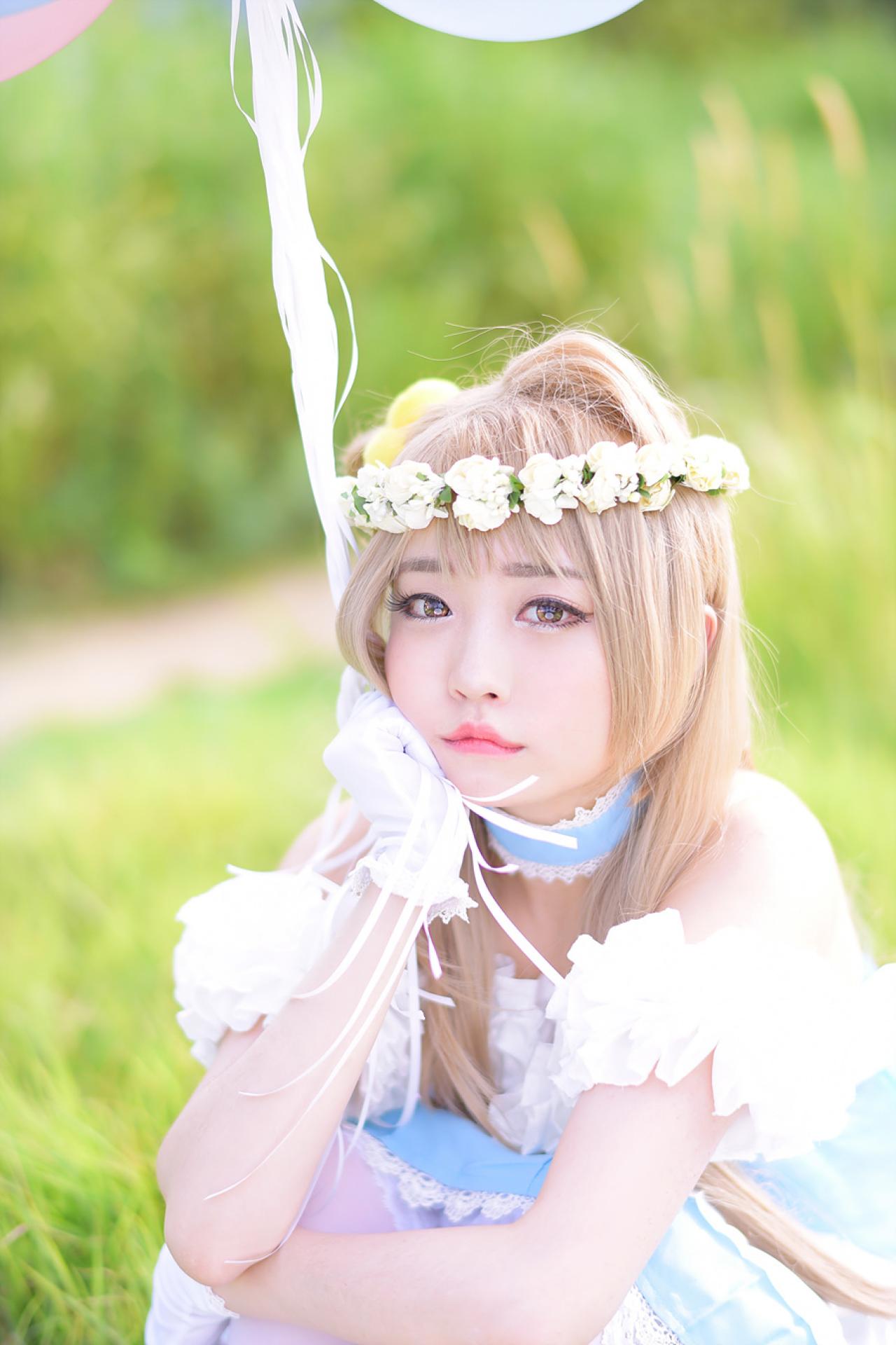 兔娘tomia扮南小鸟右手拿着气球，蹲在草地上，右手撑着下巴