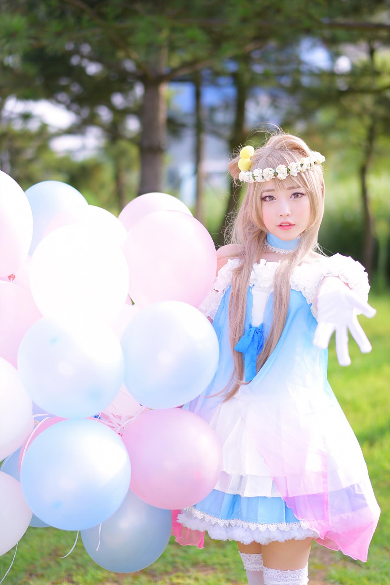 兔娘tomia扮南小鸟右手拿着气球，伸出左臂，左手五指张开，站在林间草地上