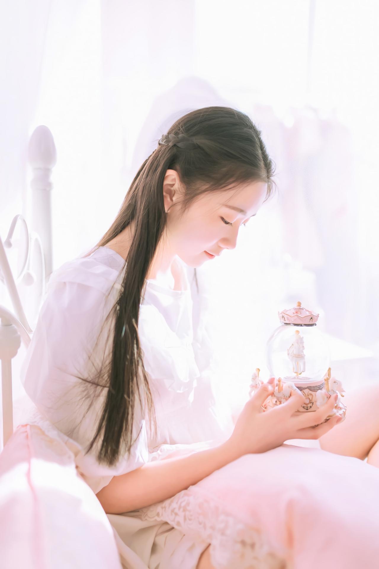 黑长直萌妹子坐在粉色床上 双手捧水晶球音乐盒