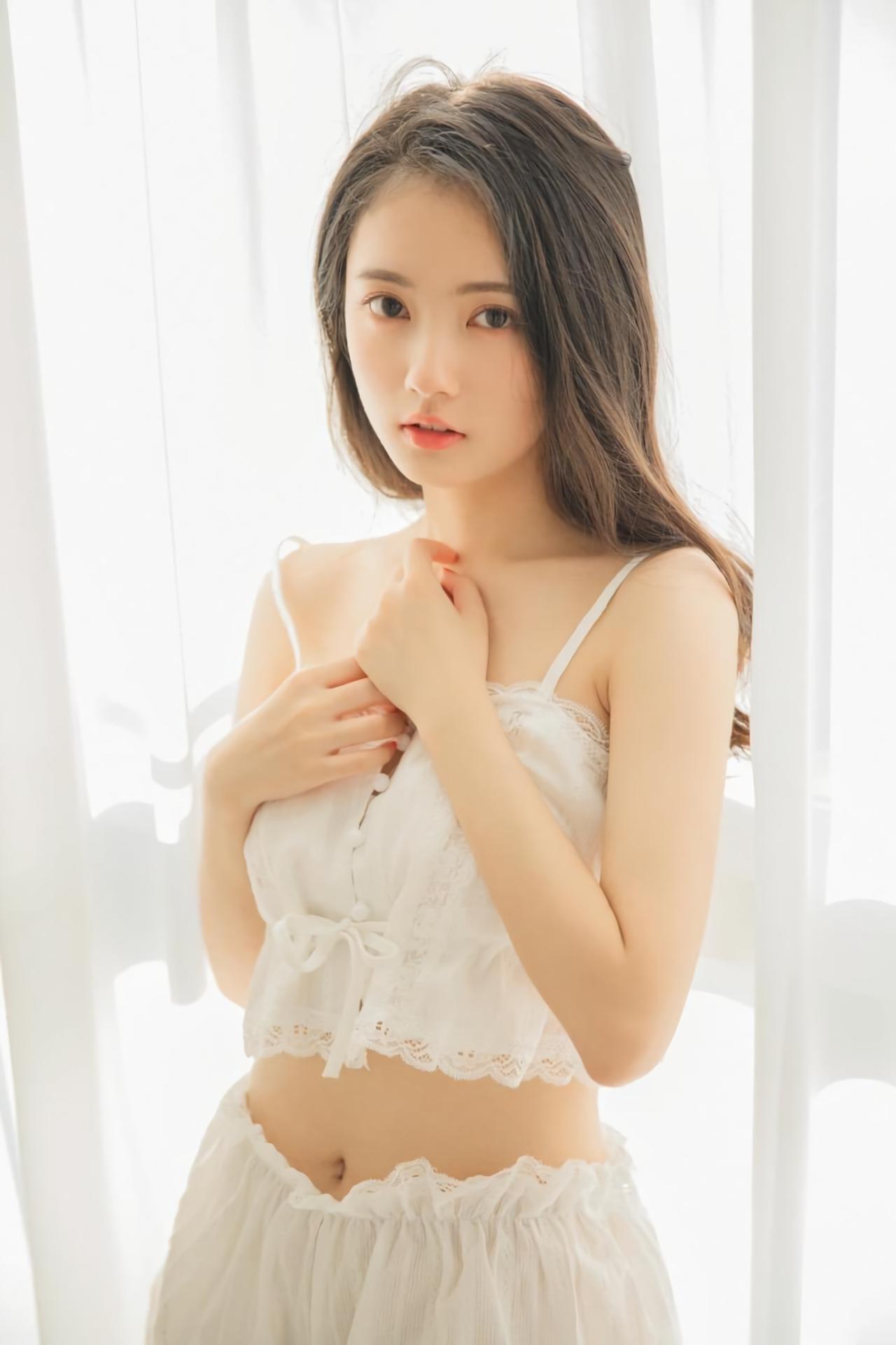 少女靠在白色窗帘，双手叠放在胸前，上半身照