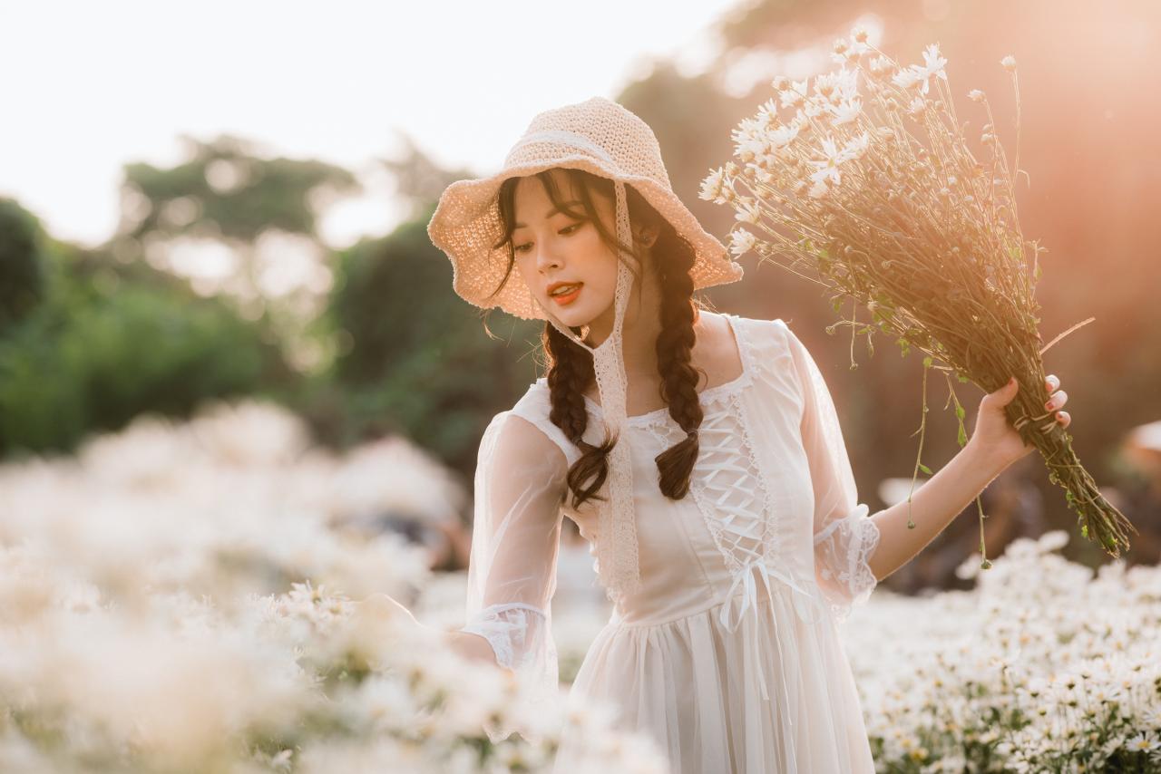 双马尾麻花辫穿着白色连衣裙花戴着草帽少女左手手持一束雏菊，漫步在雏菊的花海中 正面照 站姿