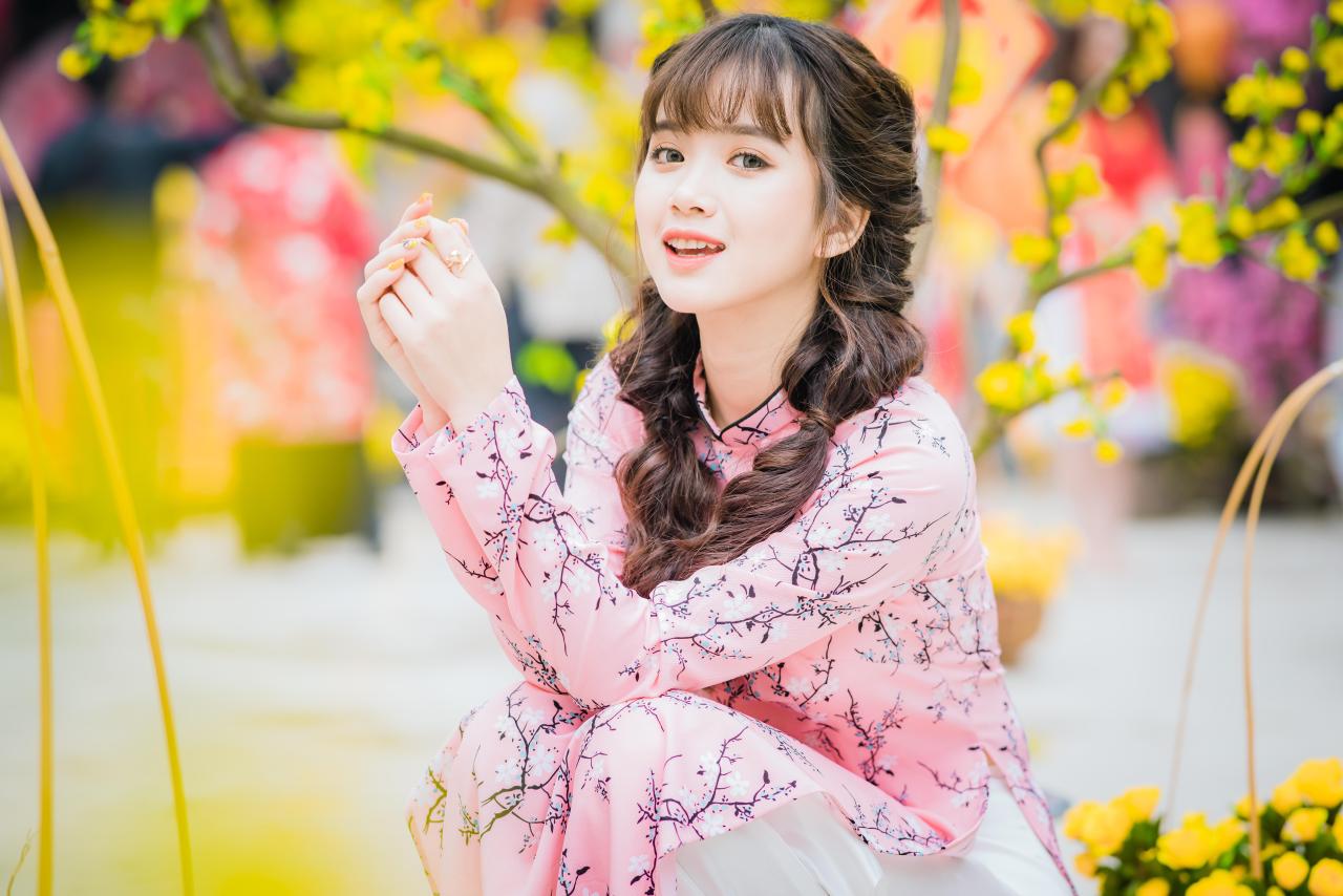 棕色双马尾卷发，齐刘海儿，穿着粉色旗袍白色长裤的少女 蹲姿 上半身照 4/3侧面照 横幅 咧嘴露齿微笑 抬头 双手握拳捧在胸前 腊梅 黄梅 花篮