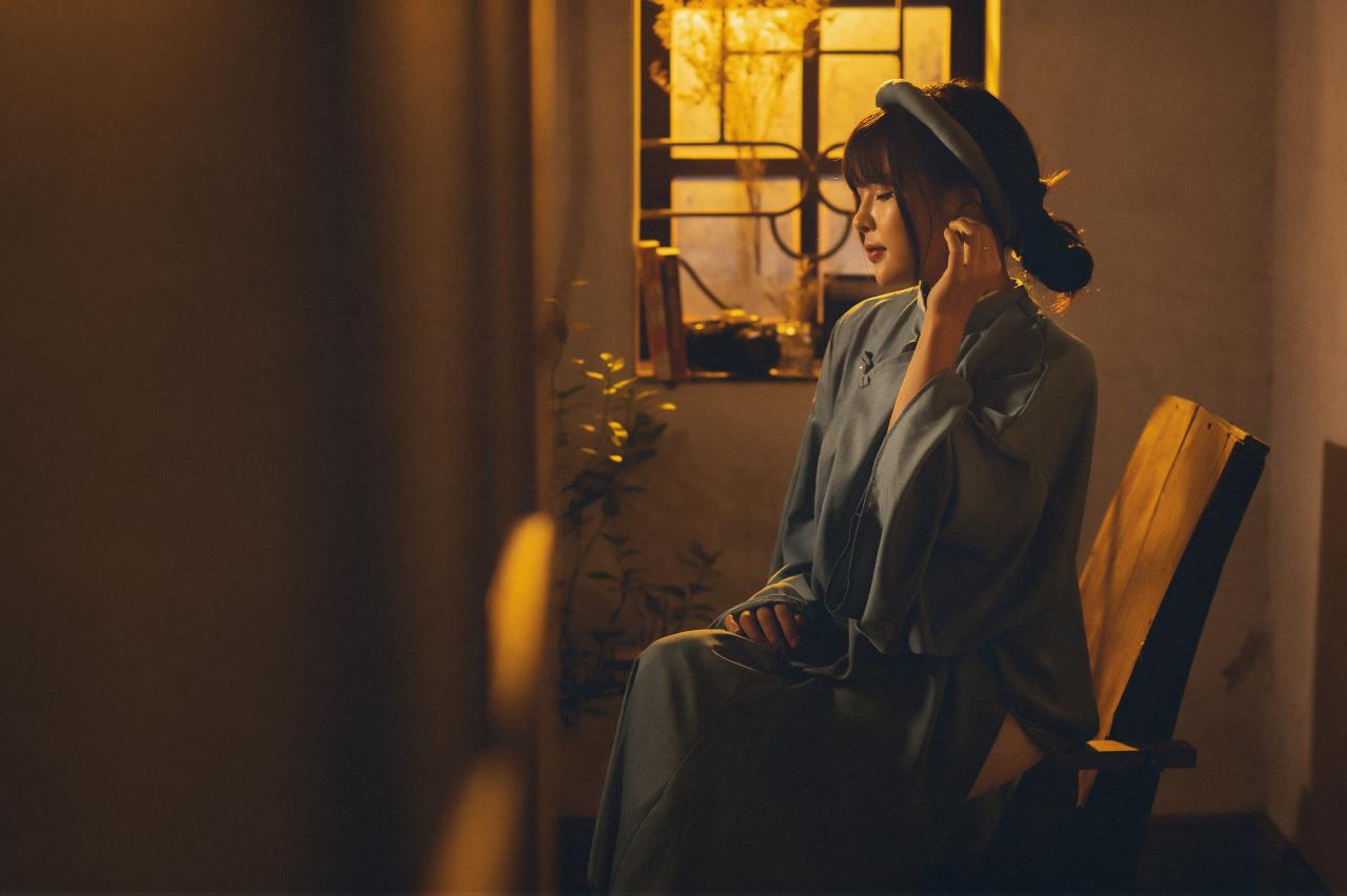 黄昏老屋窗边穿着蓝色越南长袄奥黛少女靠坐在椅子的扶手上，戴着蓝色发箍，轻抚耳垂，4/3 斜侧面照 横幅 全身照